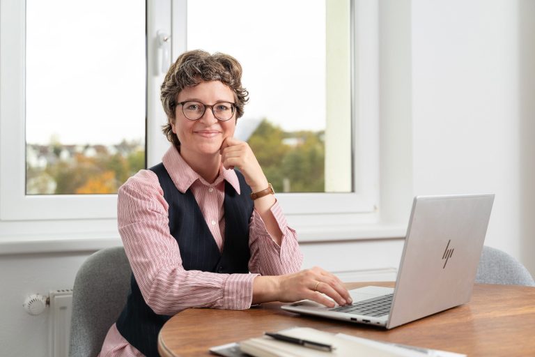 Anne Breitenberger, Lektorin Anne Breitenberger, Lektorin, am Laptop sitzend, schaut in die Kamera